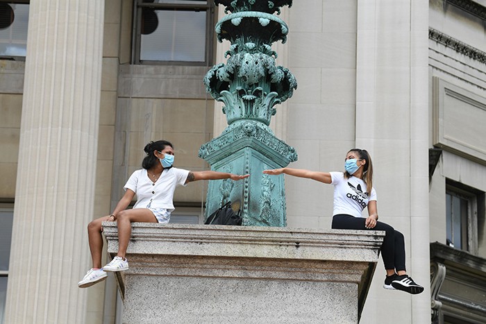 Two students sitting on Columbia University's campus wearing protective face masks.