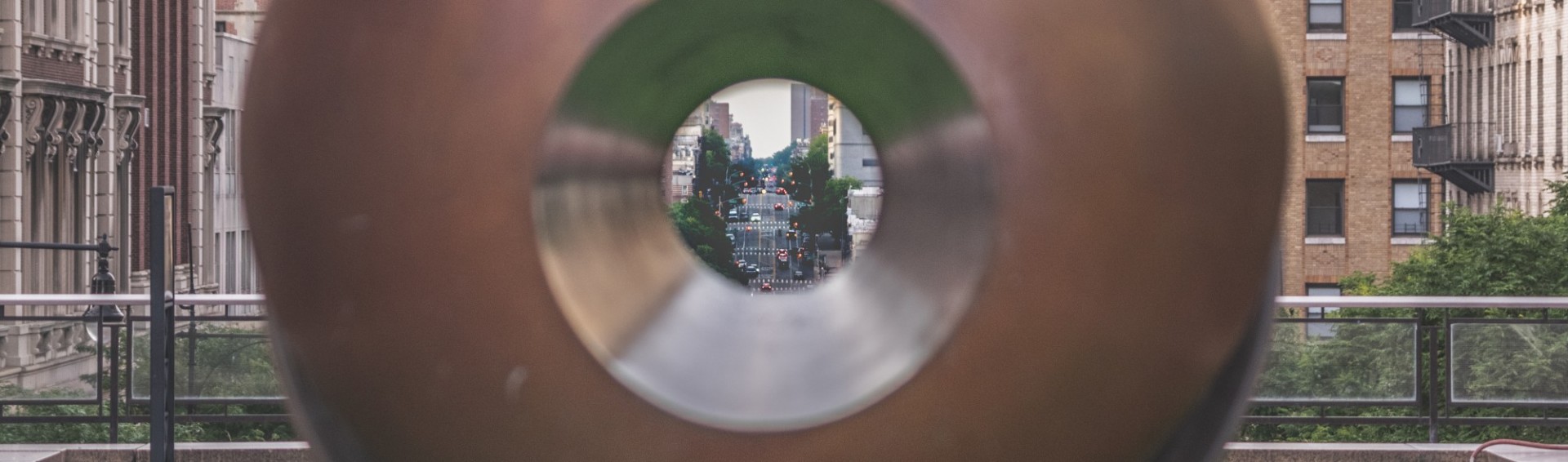 A view of Amsterdam Avenue through the center of a sculpture on Remsen Plaza